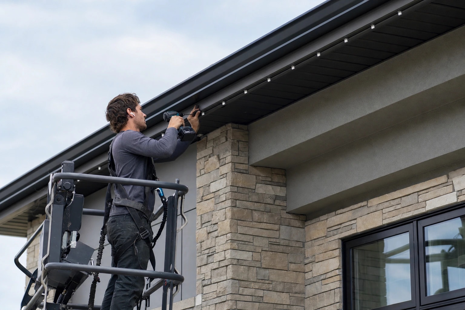 Professional installer mounting permanent LED lighting beneath a home's eaves from a secured work platform